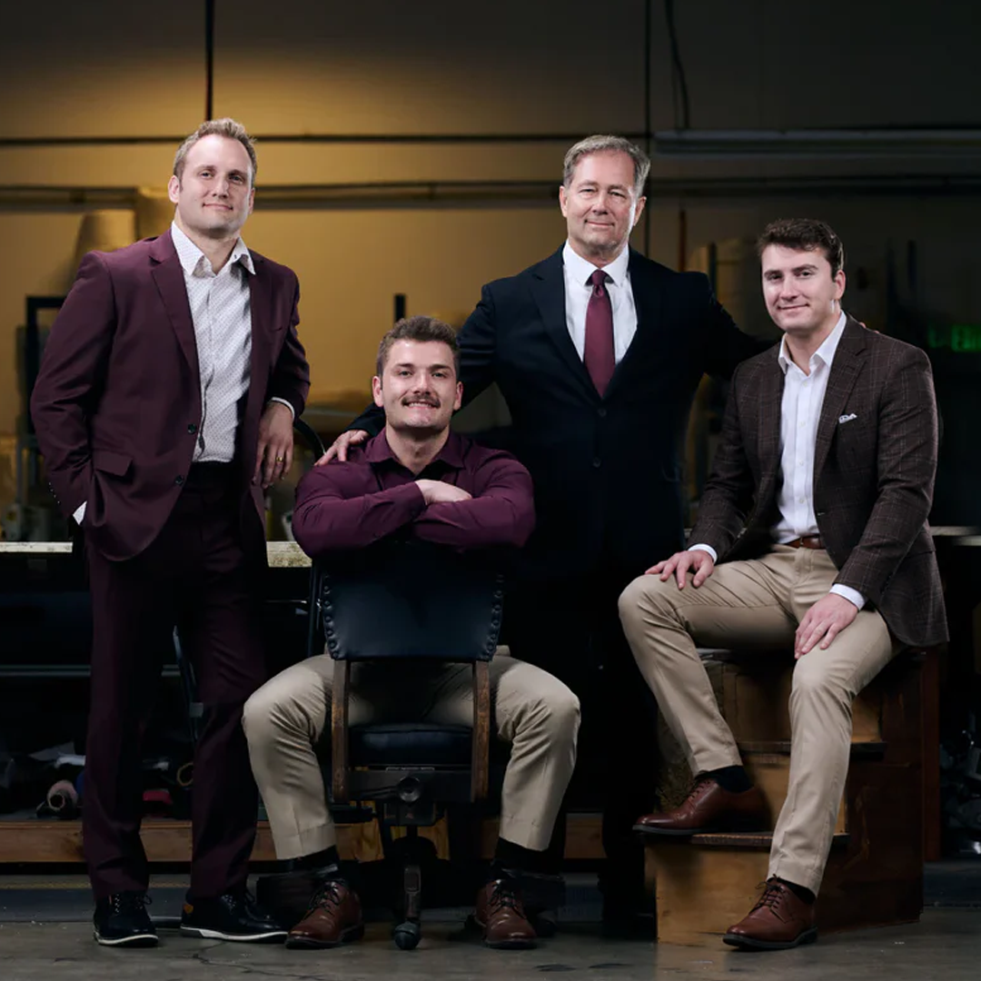 Four men in business attire posing together in a workshop setting