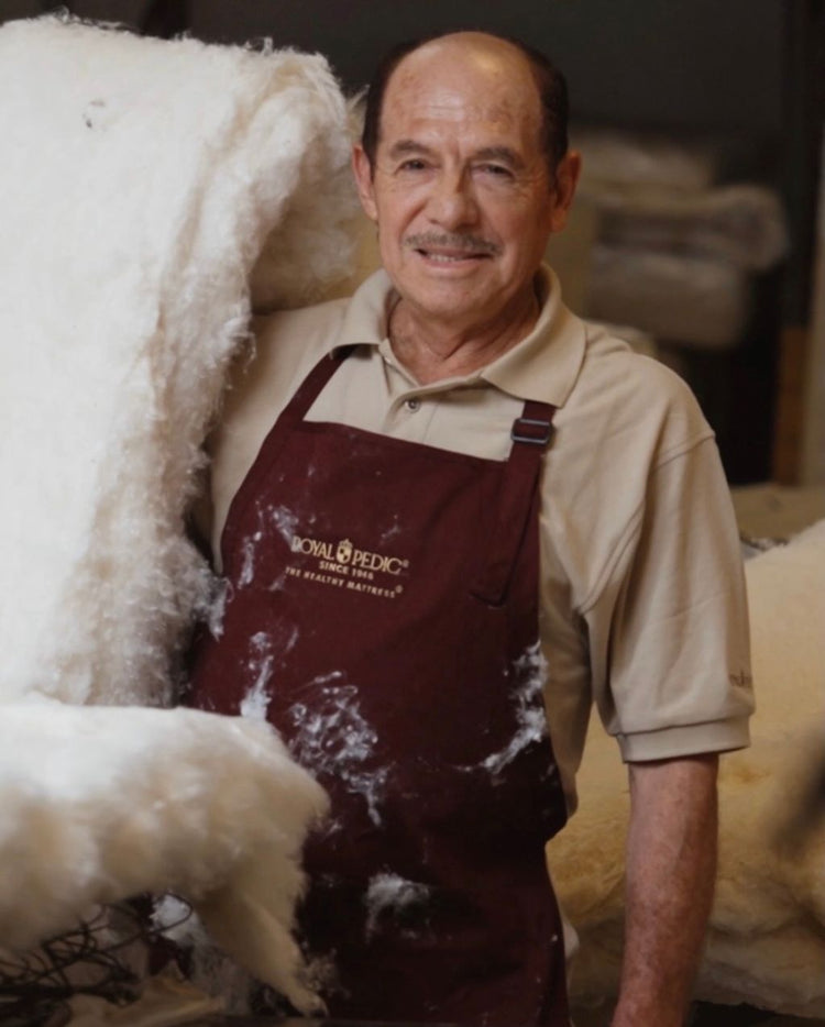 Craftsman wearing a Royal Pedic apron holding a large bundle of white cotton batting in a workshop