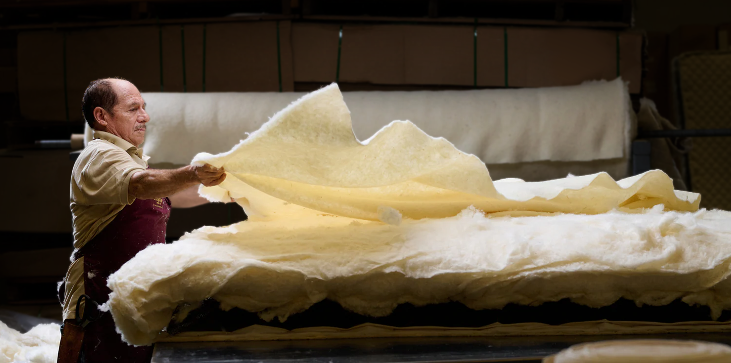 Worker layering natural wool batting onto a mattress in a workshop