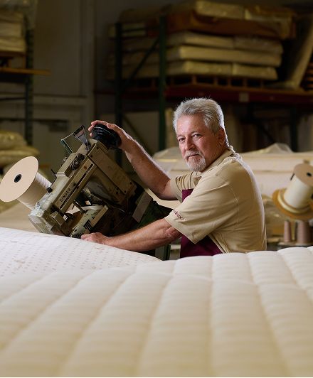 Craftsman using a Singer industrial sewing machine to stitch a mattress in a factory setting