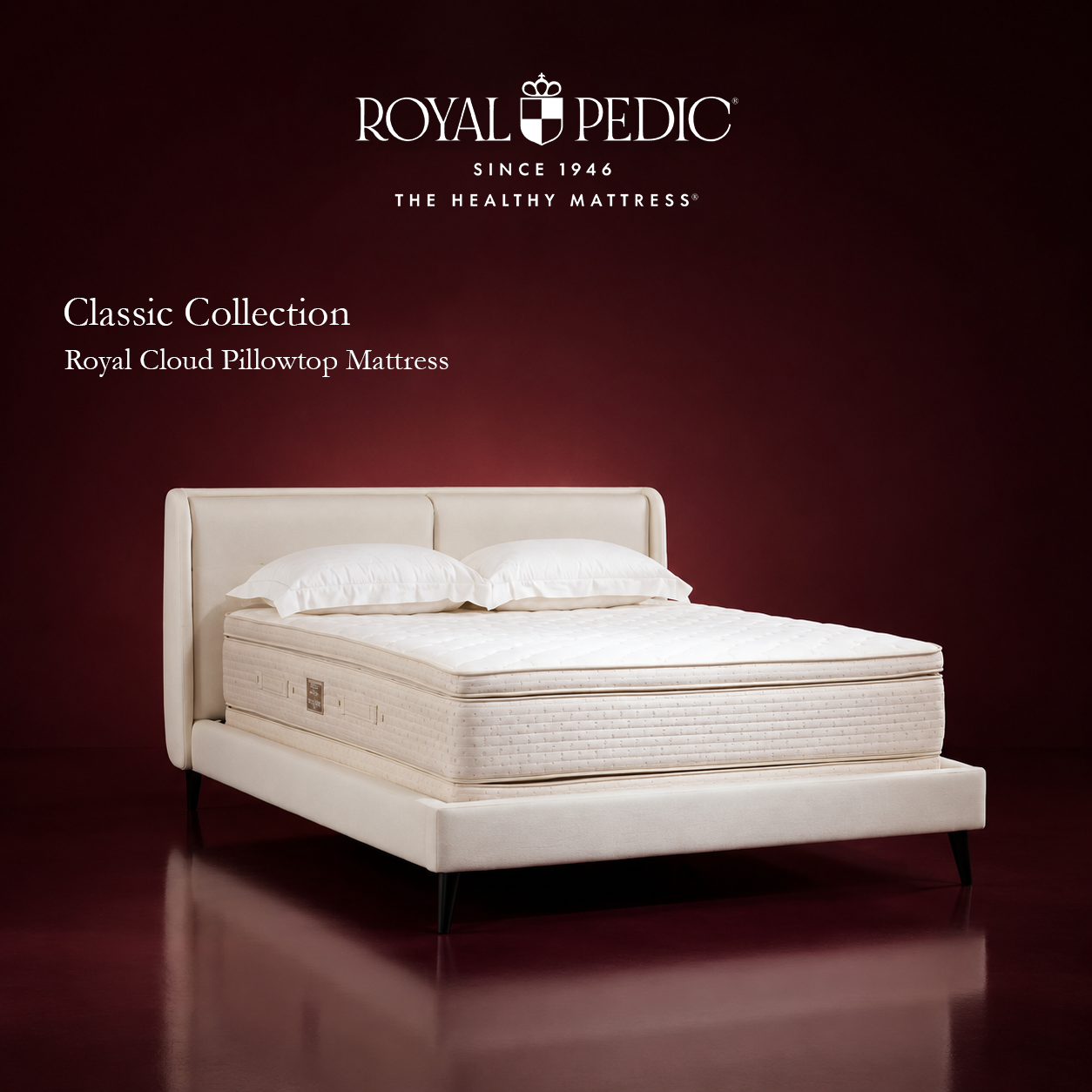 Royal Pedic Royal Cloud Pillowtop Mattress on a cream upholstered bed frame with two white pillows against a dark red background