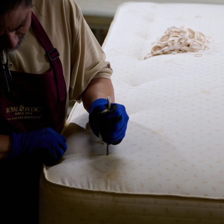 Royal-Pedic craftsman wearing blue gloves hand tufting a mattress with a needle and thread