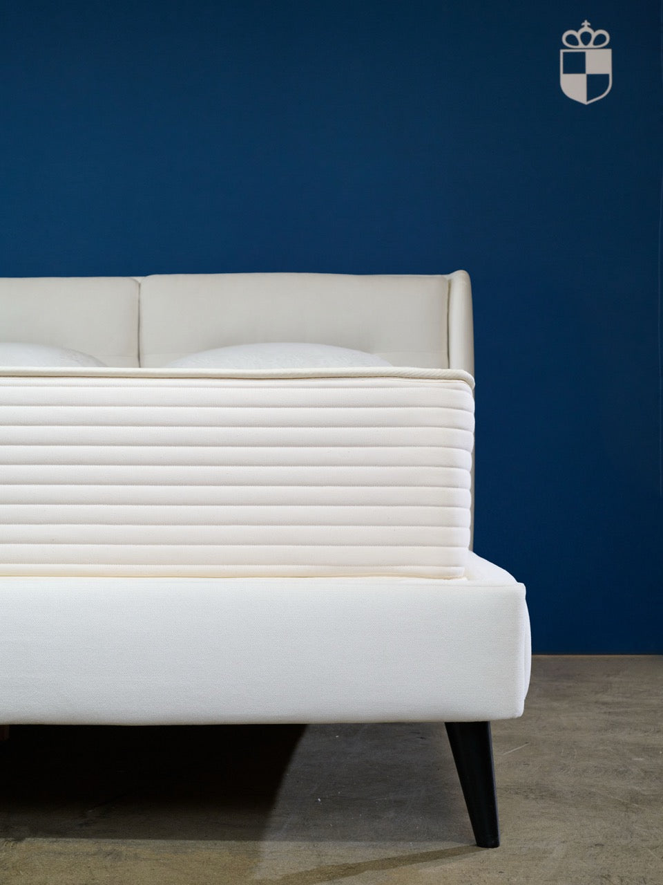 Royal-Pedic Mattress Nature Spring mattress on a white bed frame with a blue wall background.