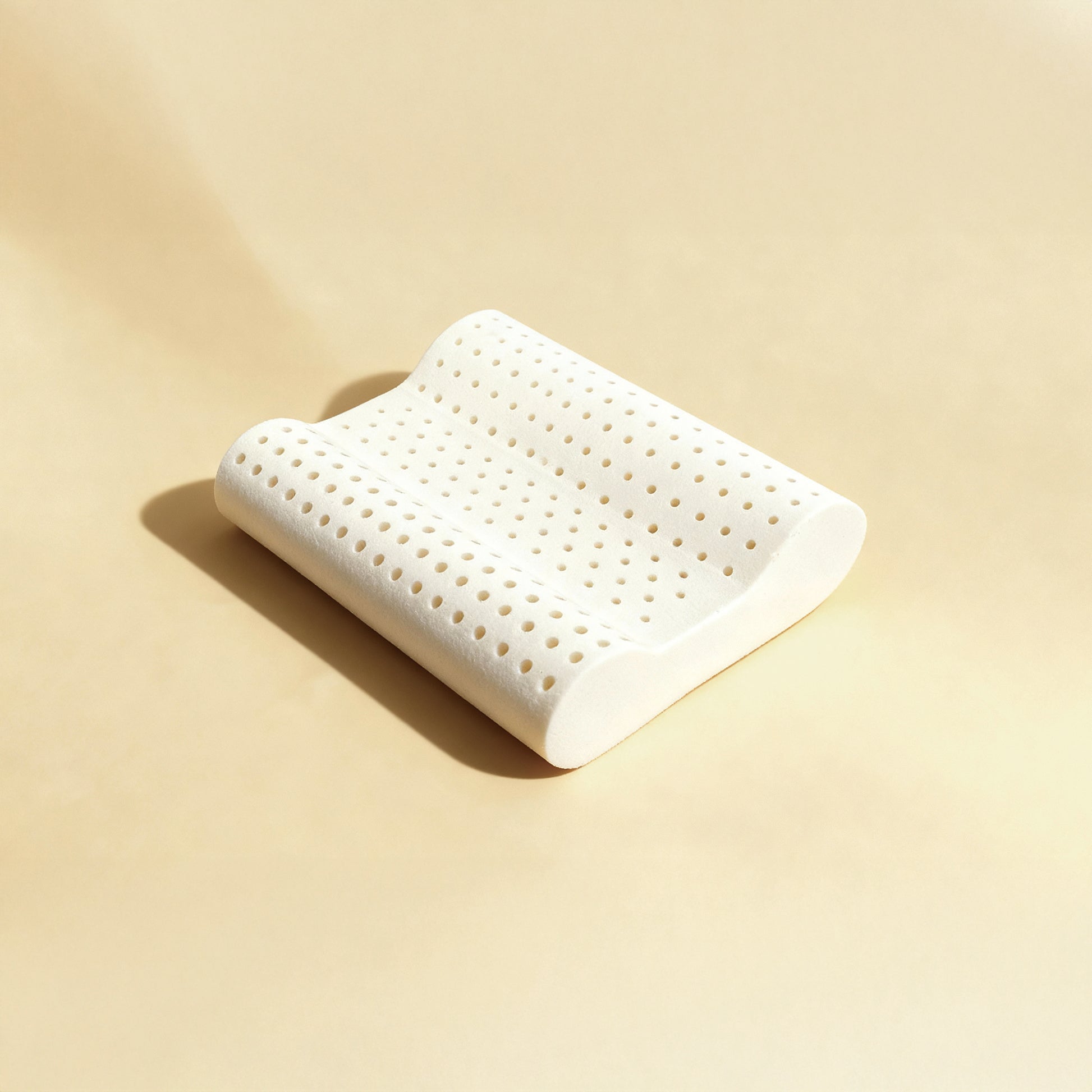 Royal-Pedic Mattress Sleepland Contoured Latex Pillow, a white, perforated pillow with a wavy, ergonomic shape, on a light tan background.